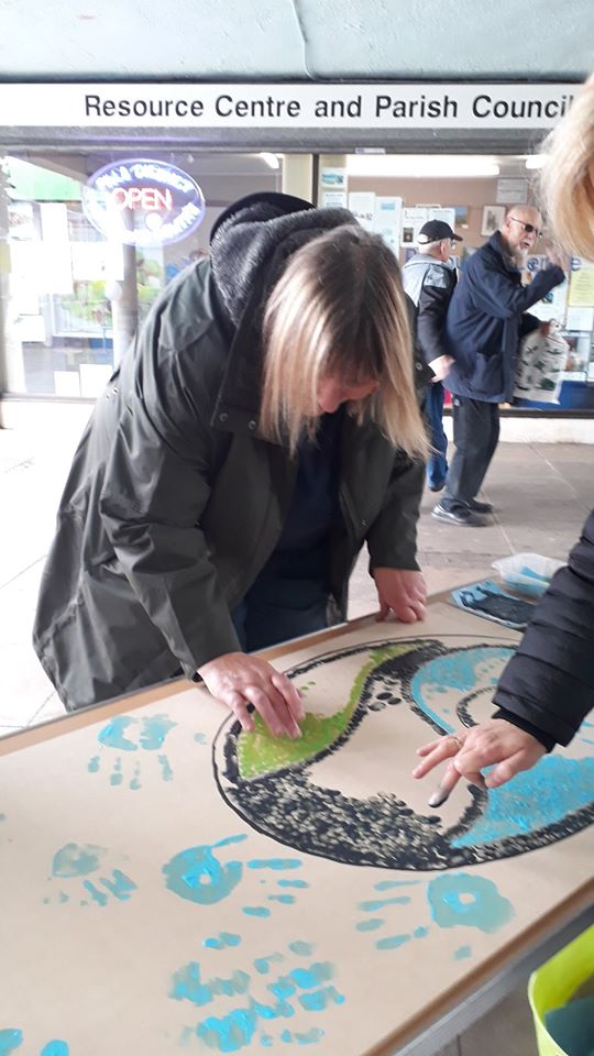 A woman adds colour to a large artwork on a table at a community centre event.